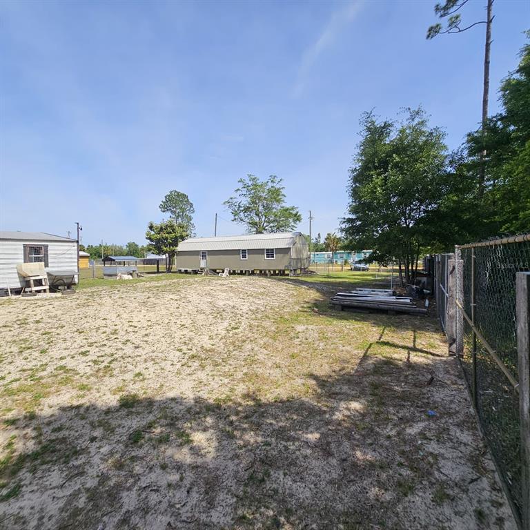 A sandy backyard features a long, light-colored shed and a chain-link fence — 12132 PINERIDGE ROAD, FOUNTAIN, FL