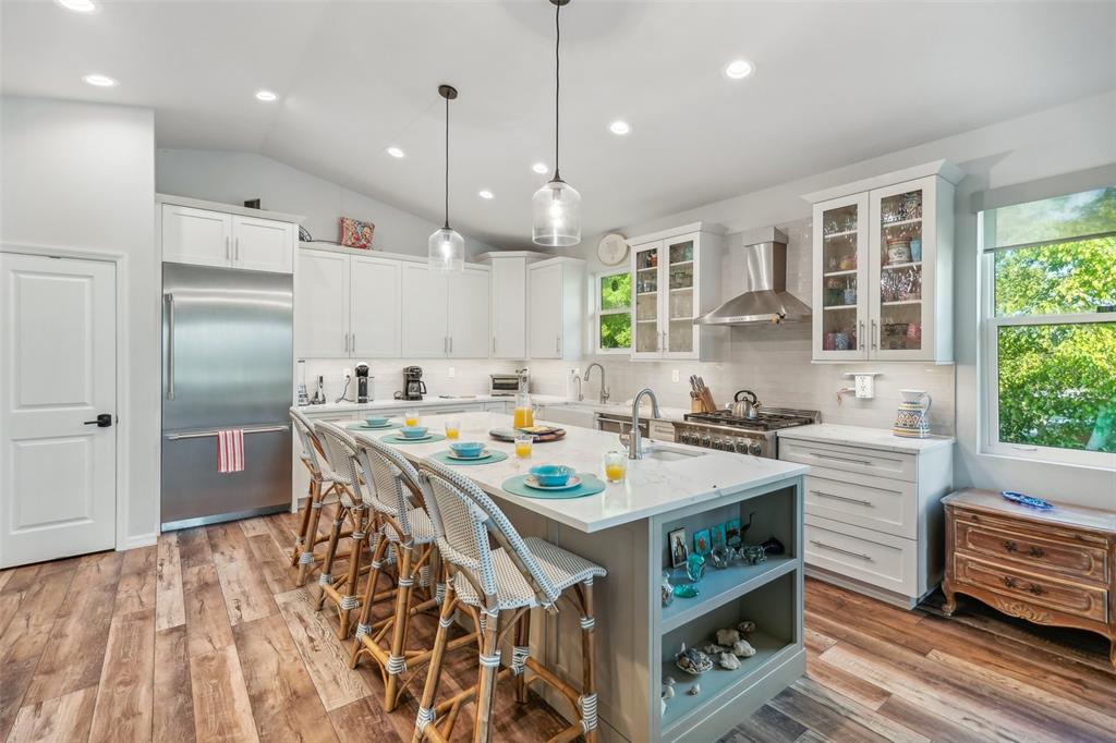 A bright kitchen features white cabinetry, a large central island with bar seating, and wood-look flooring — 501 CHANNEL LANE, LONGBOAT KEY, FL