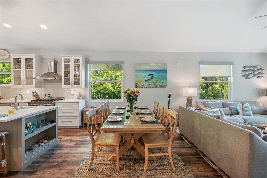 An open-concept kitchen, dining area, and living room featuring wood floors and white cabinetry — 501 CHANNEL LANE, LONGBOAT KEY, FL