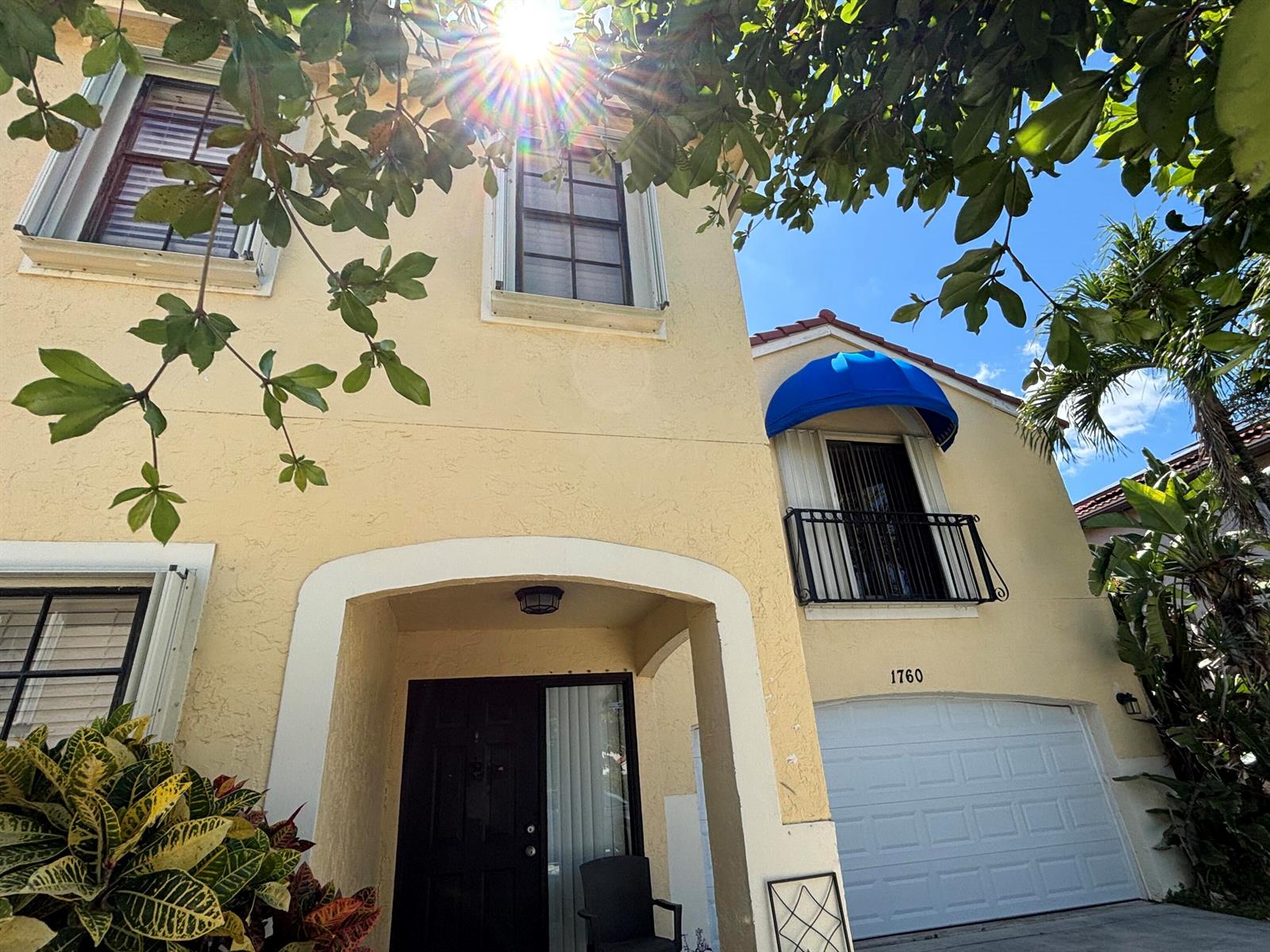 A two-story yellow stucco house features a black front door, a garage, and a blue awning — 1760 Shoreside Circle, Wellington FL 33414, WELLINGTON, FL
