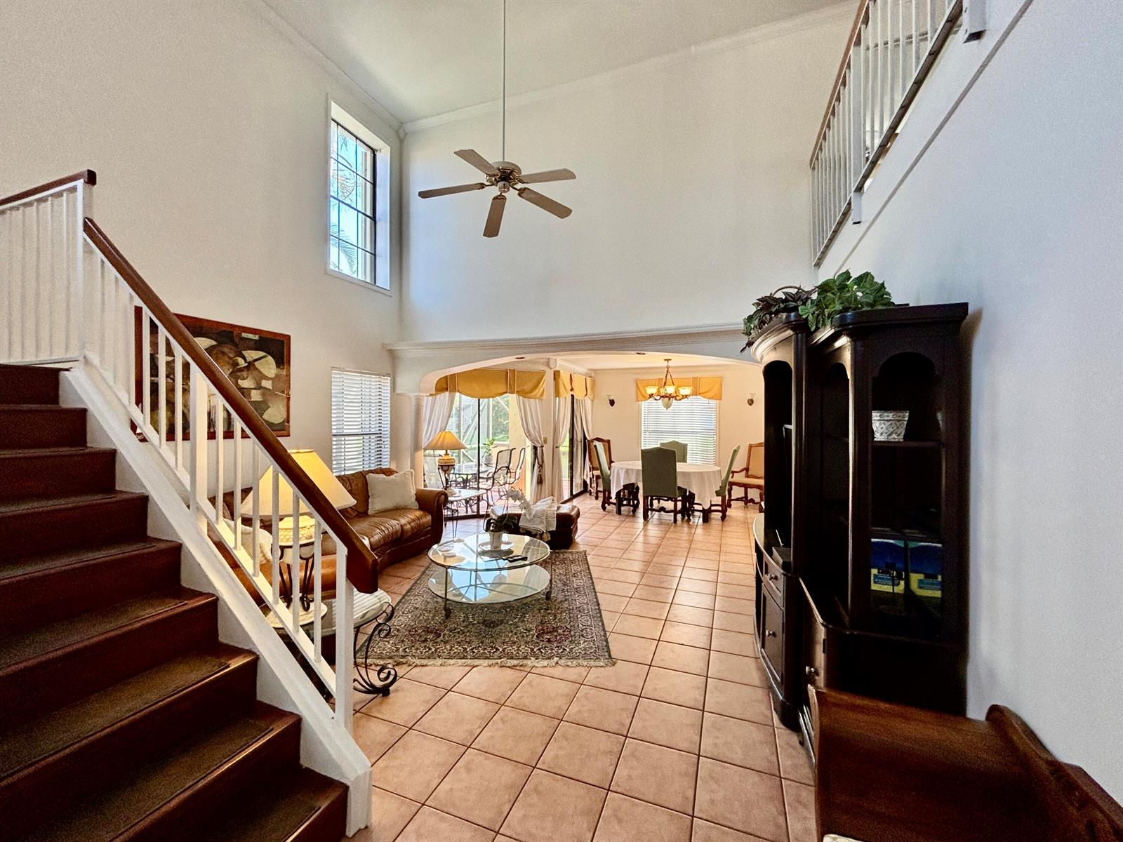 A high-ceilinged living and dining area features tile floors, a staircase, and large windows — 1760 Shoreside Circle, Wellington FL 33414, WELLINGTON, FL