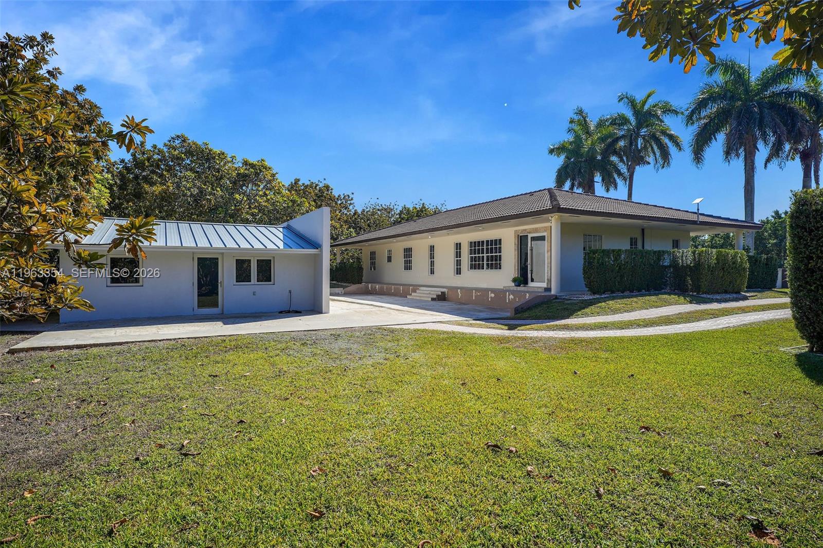 A single-story house with a metal-roofed addition and a large lawn under a blue sky — 19955 SW 186th St, Miami FL 33187, MIAMI, FL