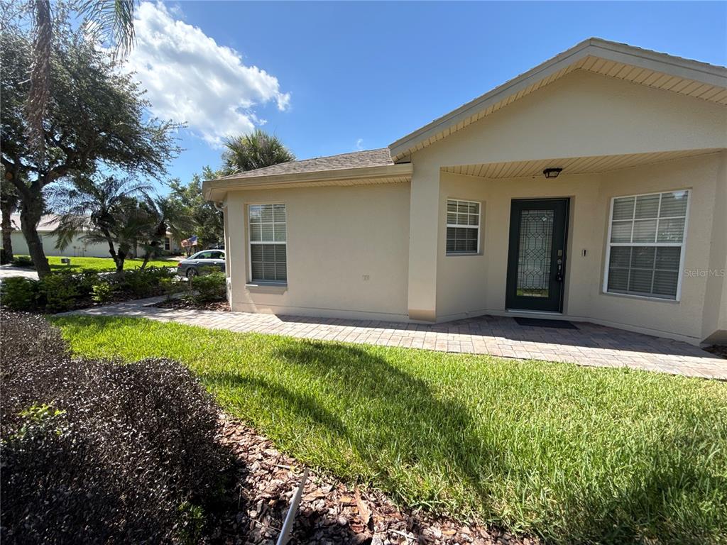 A single-story house exterior features a paved walkway, tan stucco walls, and a dark door — 674 VINEYARD WAY, POINCIANA, FL