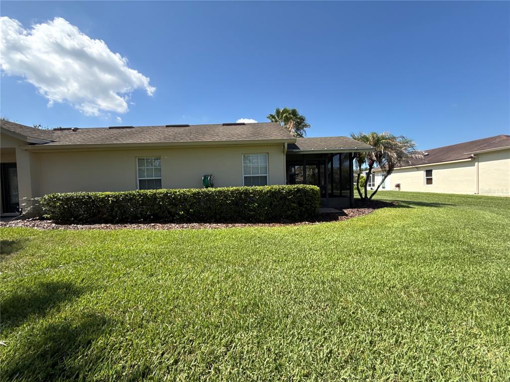 A view of a house exterior with a green lawn, hedge, and screened-in patio — 674 VINEYARD WAY, POINCIANA, FL