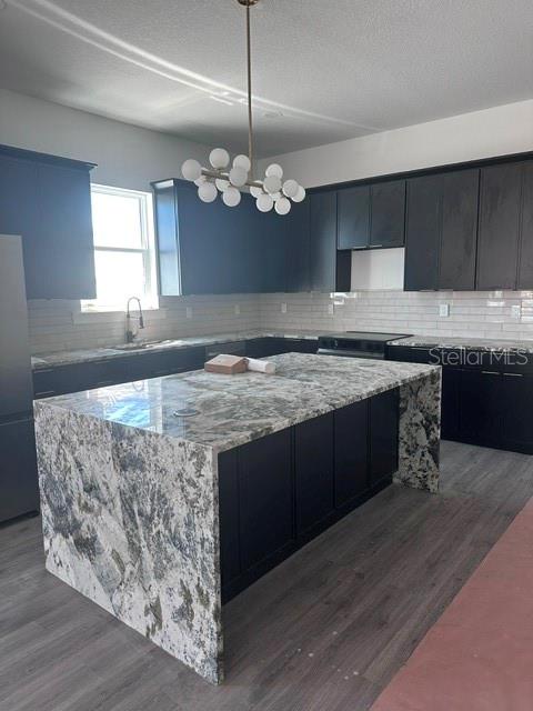 A modern kitchen features dark cabinets, a large granite waterfall island, and a globe chandelier — 1531 29TH AVENUE N, ST PETERSBURG, FL