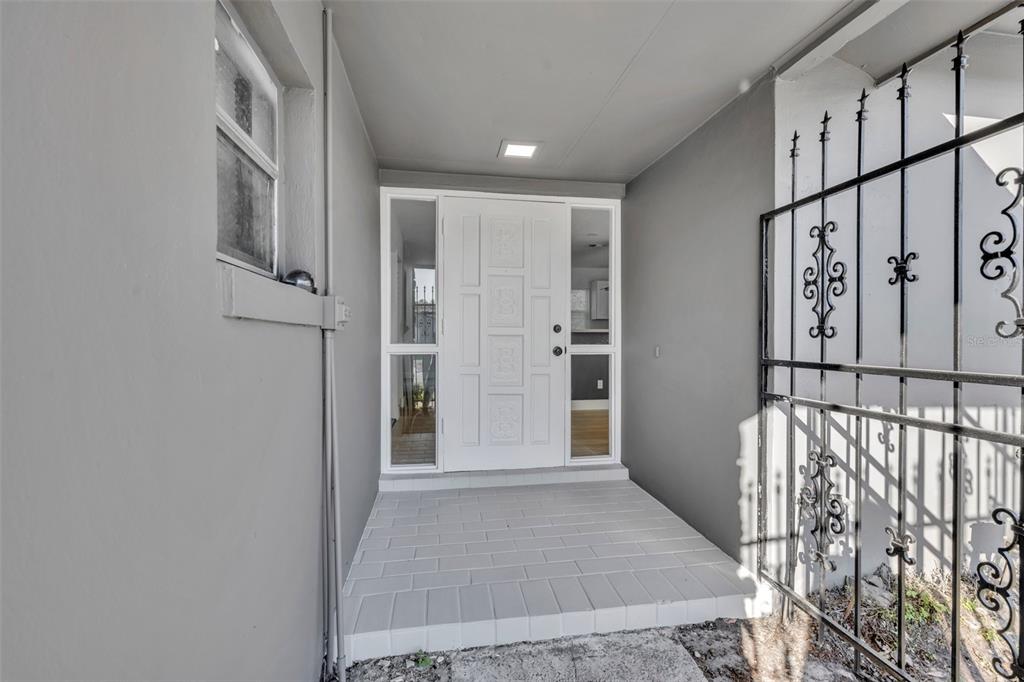 A white front door with sidelights sits on a tiled porch next to metal security bars — 2216 CHERBOURG COURT, ORLANDO, FL