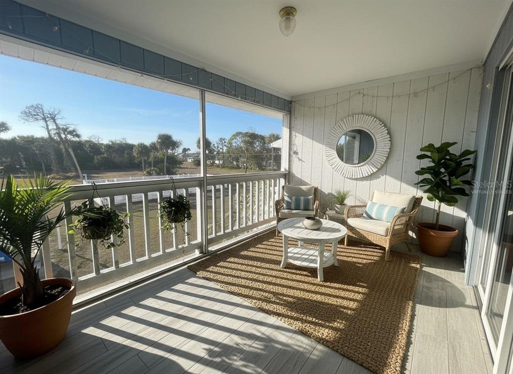 A screened-in balcony features a woven rug, wicker chairs, a round table, and outdoor views — 200 ROTONDA BOULEVARD W UNIT A4, ROTONDA WEST, FL