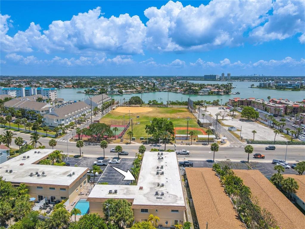 An aerial view shows a multi-story apartment building with a parking lot and nearby fields — 9050 BLIND PASS ROAD UNIT 9, ST PETE BEACH, FL