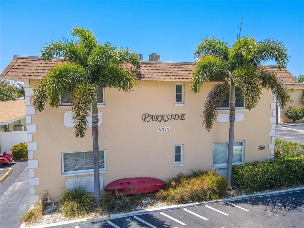 A two-story tan apartment building features palm trees and a red kayak leaning against it — 9050 BLIND PASS ROAD UNIT 9, ST PETE BEACH, FL