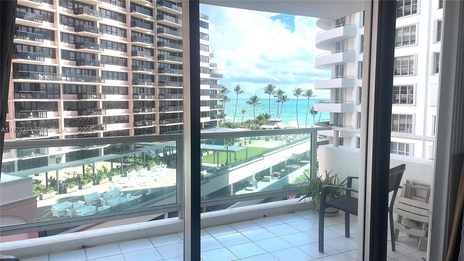 A balcony with white tile flooring overlooks a pool deck, palm trees, and the ocean — 5161 Collins Ave # 603, Miami Beach FL 33140, MIAMI BEACH, FL