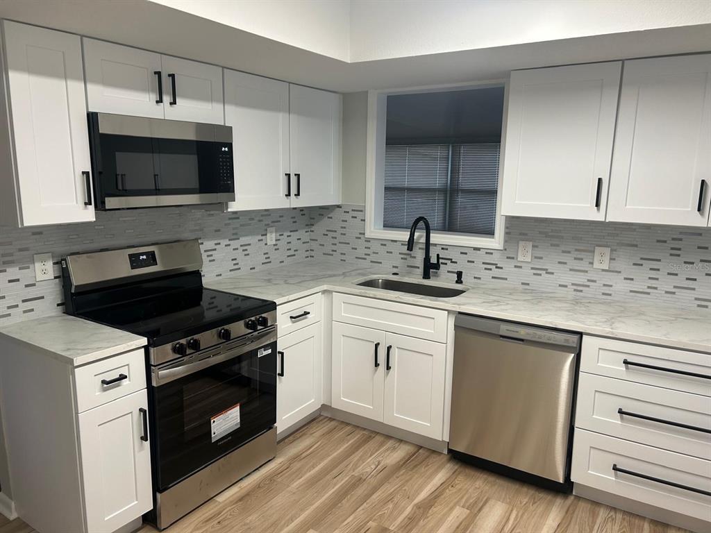 A kitchen features white cabinets, stainless steel appliances, marble-look countertops, and a mosaic tile backsplash — 5102 PEACHGREEN COURT, TAMPA, FL