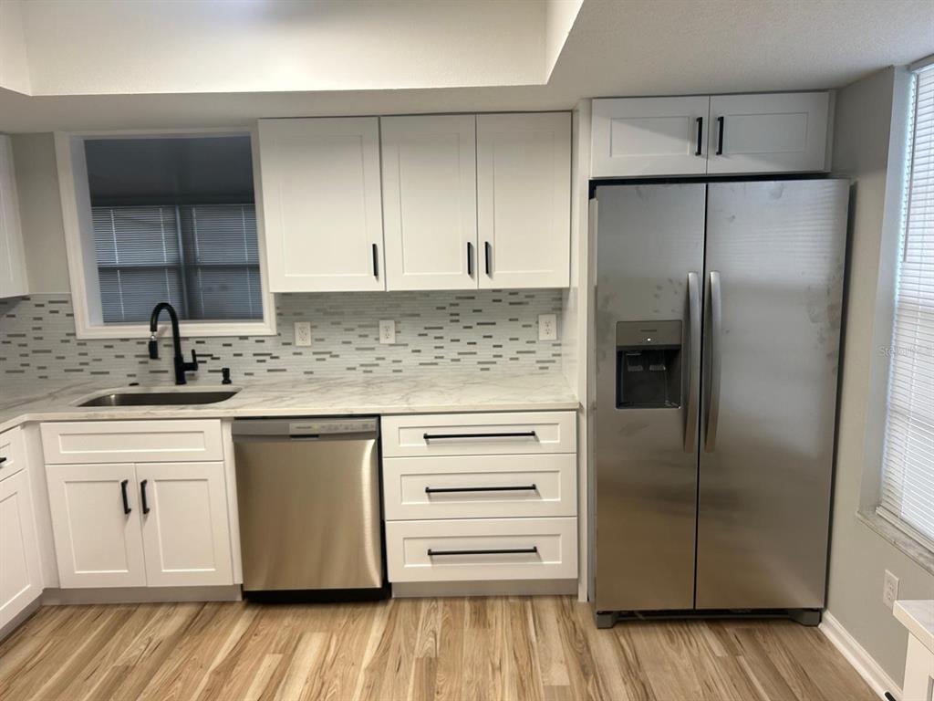 A kitchen features white cabinets, stainless steel appliances, a marble-look countertop, and a mosaic backsplash — 5102 PEACHGREEN COURT, TAMPA, FL