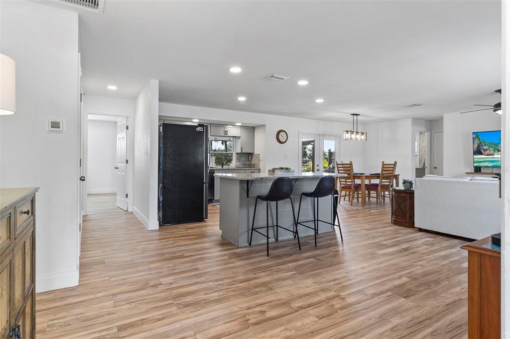 An open-concept kitchen and living area featuring a central island, bar stools, and wood flooring — 20495 ALBURY DRIVE, PORT CHARLOTTE, FL