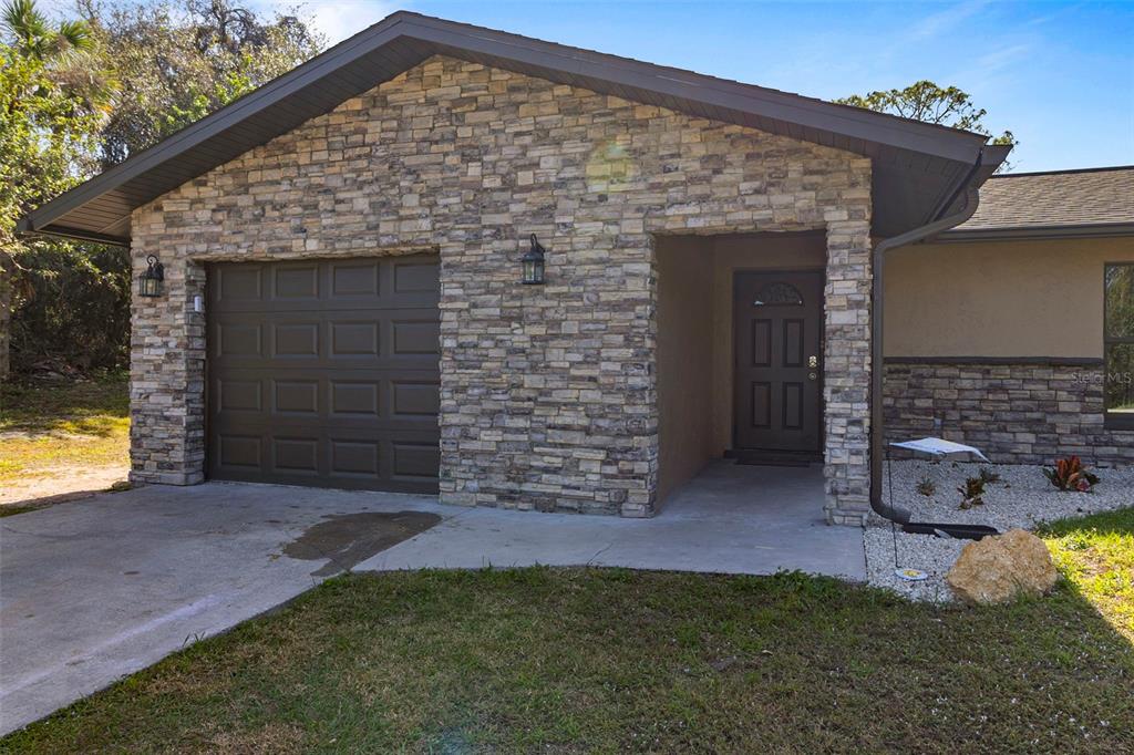 A single-story house exterior features a stone facade, a brown garage door, and a front entrance — 20495 ALBURY DRIVE, PORT CHARLOTTE, FL