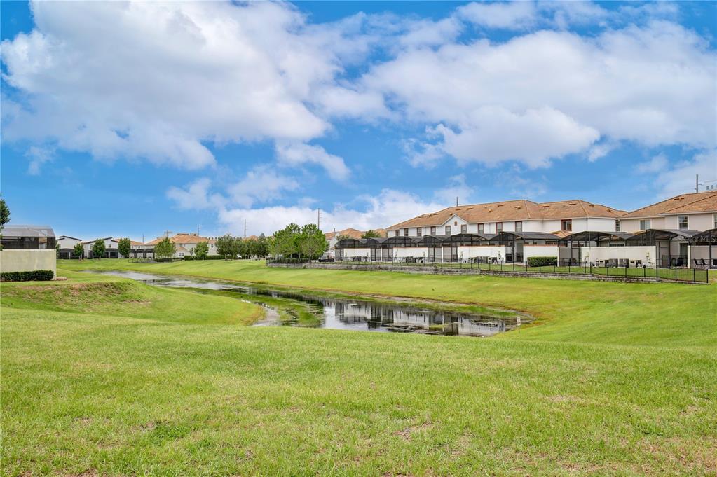 A grassy lawn slopes down toward a small pond behind a row of suburban houses — 3062 GATSBY STREET, KISSIMMEE, FL