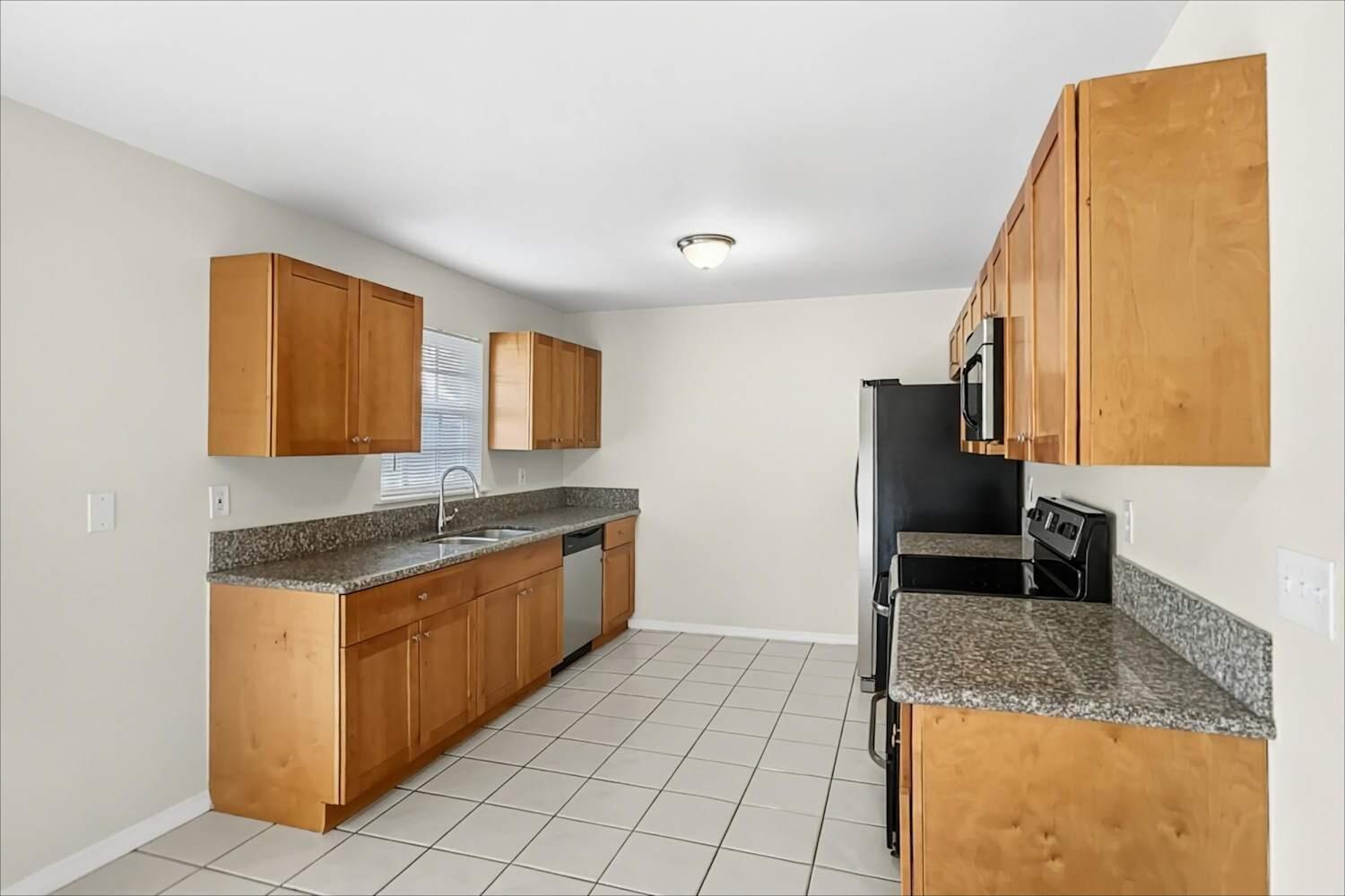 A kitchen features light wood cabinets, granite countertops, black appliances, and white tile flooring — NORTH PALM BEACH, FL