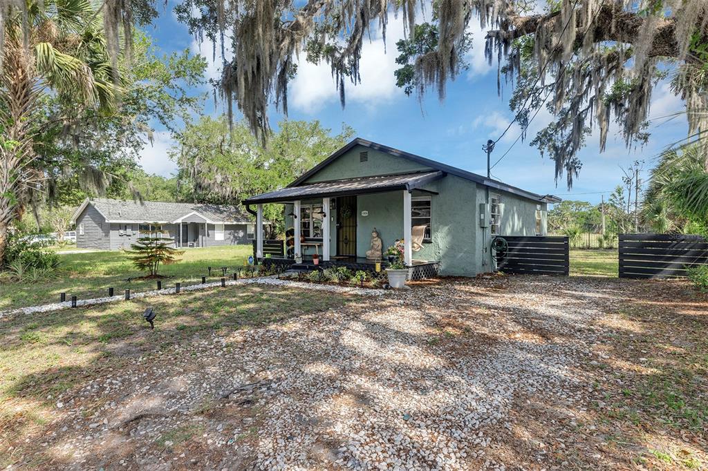 A single-story green house with a front porch sits on a gravel lot under trees — 1806 REDDING PLACE, SANFORD, FL