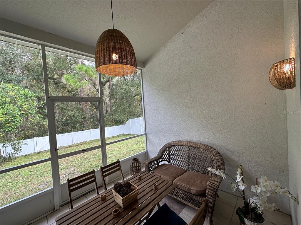 A screened-in porch features wicker furniture, a wooden table, and views of a backyard — 29651 BIRDS EYE DRIVE, WESLEY CHAPEL, FL