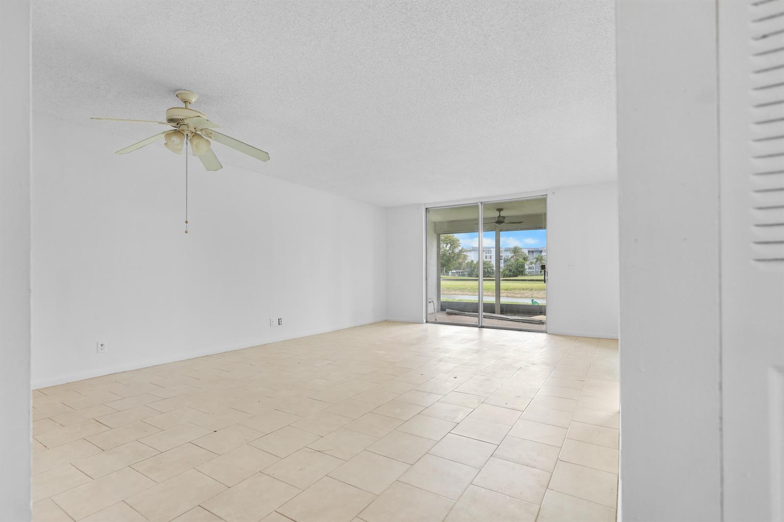 An empty living room with white walls, tile flooring, a ceiling fan, and sliding glass doors — 1460 NW 80th Avenue # 108, Margate FL 33063, MARGATE, FL