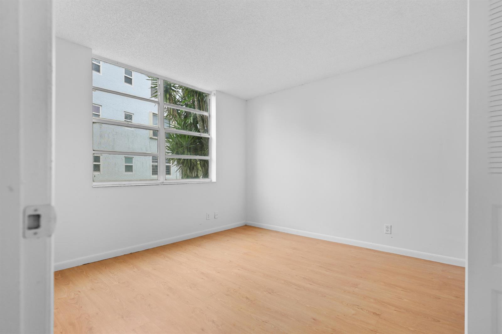 An empty bedroom features white walls, light wood-look flooring, and a large multi-pane window — 1460 NW 80th Avenue # 108, Margate FL 33063, MARGATE, FL