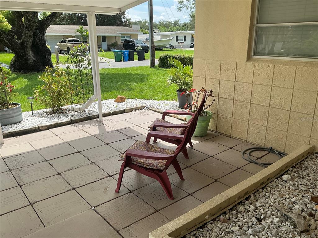 A covered patio features square concrete pavers, two red chairs, and a view of a yard — 7360 111TH STREET, SEMINOLE, FL