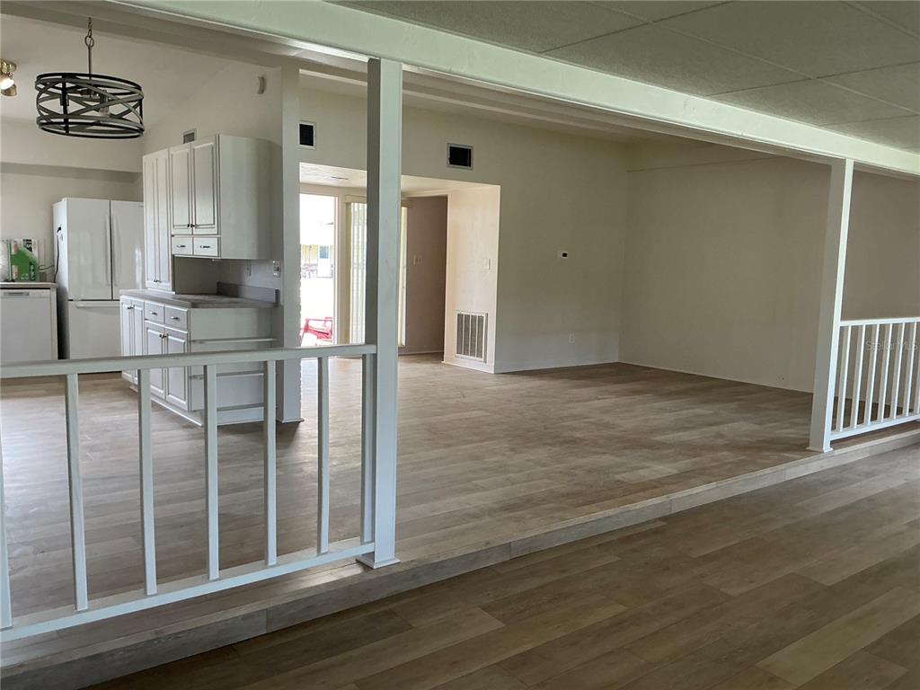 A kitchen and living area feature light wood-look flooring and a white wooden railing — 7360 111TH STREET, SEMINOLE, FL