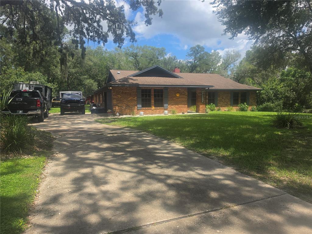 A single-story brick house with a dark roof sits behind a concrete driveway and lawn — 2417 S OAK PARK DRIVE, DELAND, FL