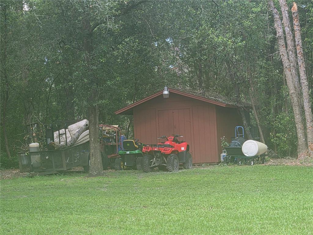A red storage shed sits in a wooded yard with a trailer, lawnmower, and ATV — 2417 S OAK PARK DRIVE, DELAND, FL