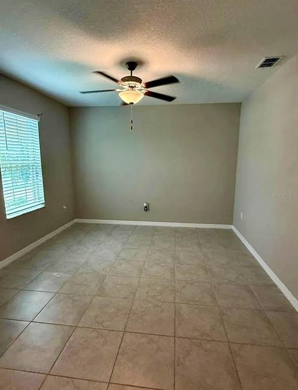 An empty room features beige walls, tile flooring, and a ceiling fan with a light — 12957 WILDFLOWER MEADOW DRIVE, RIVERVIEW, FL