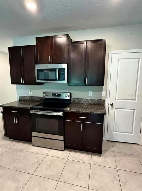 A kitchen features dark wood cabinets, stainless steel appliances, and granite countertops over tiled floors — 12957 WILDFLOWER MEADOW DRIVE, RIVERVIEW, FL