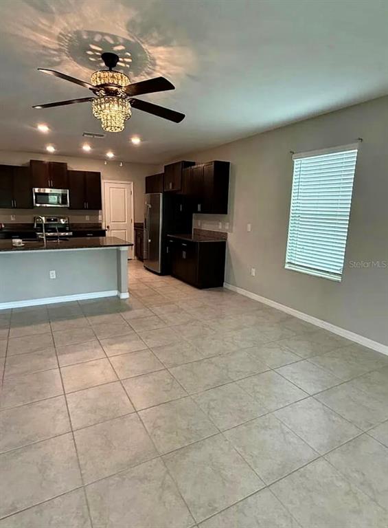 A kitchen with dark cabinets, a granite island, and tile flooring opens to a living area — 12957 WILDFLOWER MEADOW DRIVE, RIVERVIEW, FL