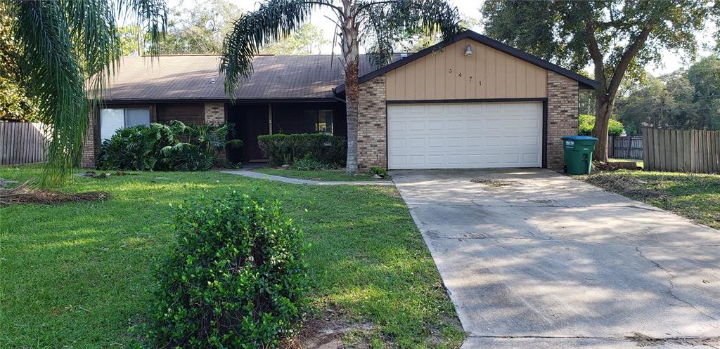 A single-story brick and wood-sided house features a two-car garage and a concrete driveway — 3471 APPLE ORCHARD DRIVE, DELTONA, FL
