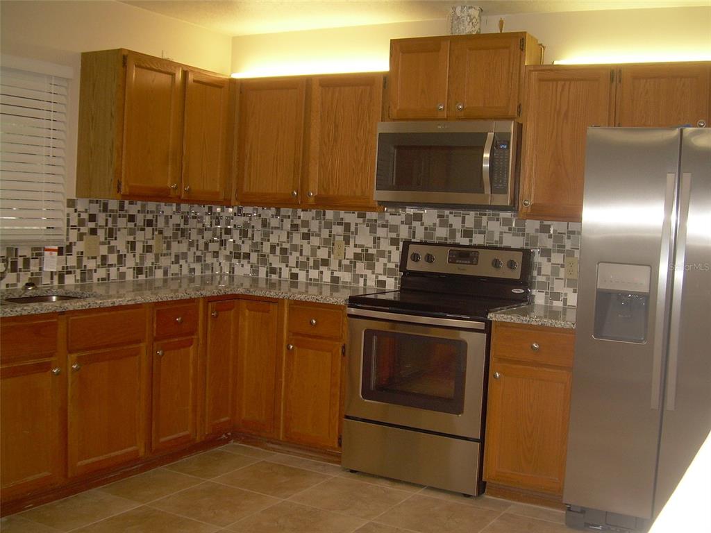 A kitchen features wood cabinets, granite countertops, stainless steel appliances, and a mosaic tile backsplash — 3471 APPLE ORCHARD DRIVE, DELTONA, FL