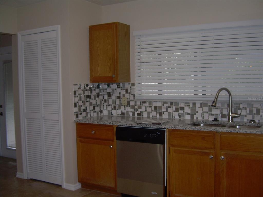 A kitchen features wood cabinets, granite countertops, a mosaic tile backsplash, and a stainless steel dishwasher — 3471 APPLE ORCHARD DRIVE, DELTONA, FL