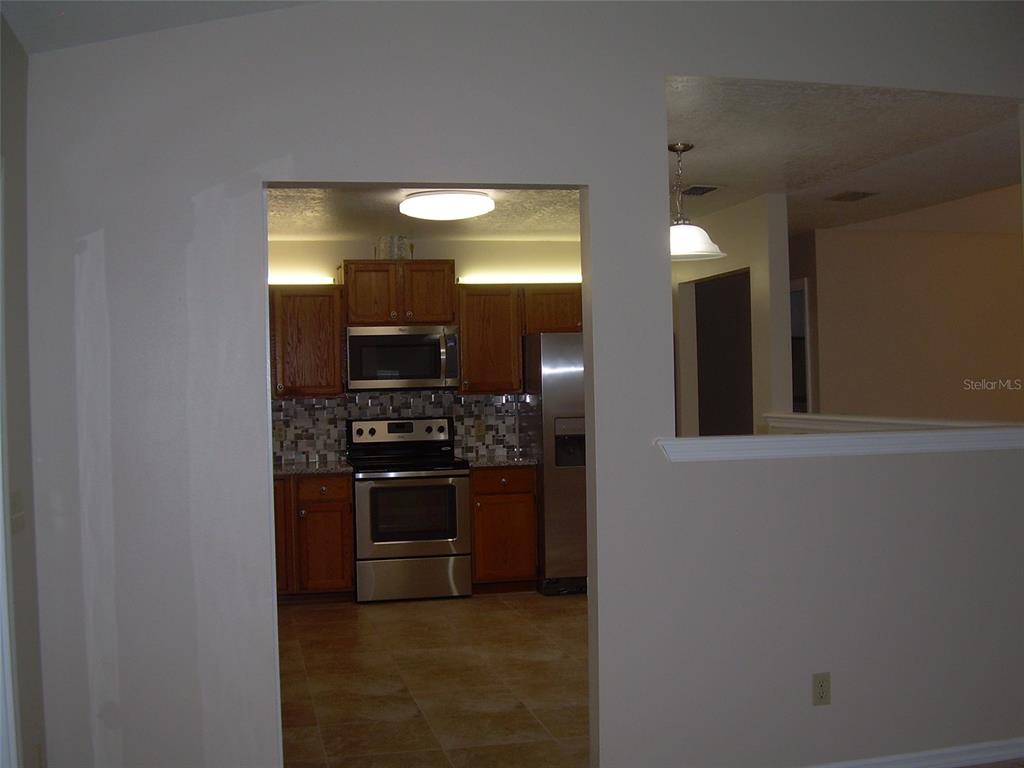 A kitchen with wood cabinets and stainless steel appliances is viewed through a wall opening — 3471 APPLE ORCHARD DRIVE, DELTONA, FL