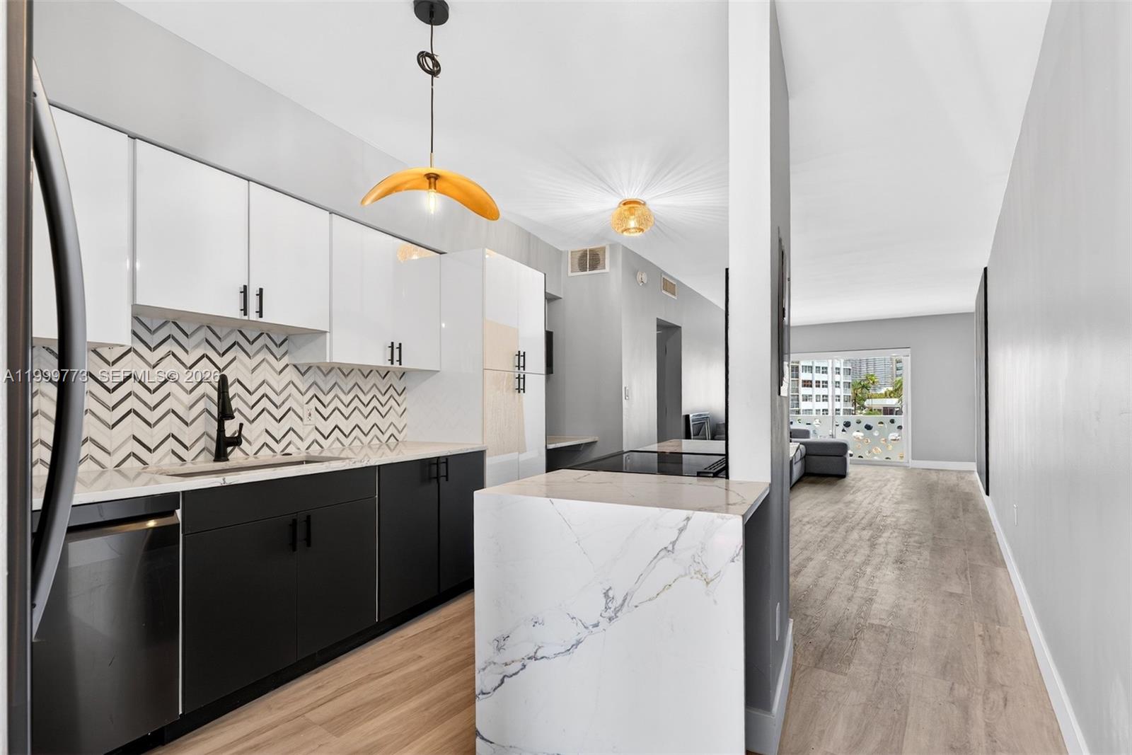 A modern kitchen features black lower cabinets, white upper cabinets, and a marble-topped island — 2500 Diana Dr # 216, Hallandale Beach FL 33009, HALLANDALE BEACH, FL
