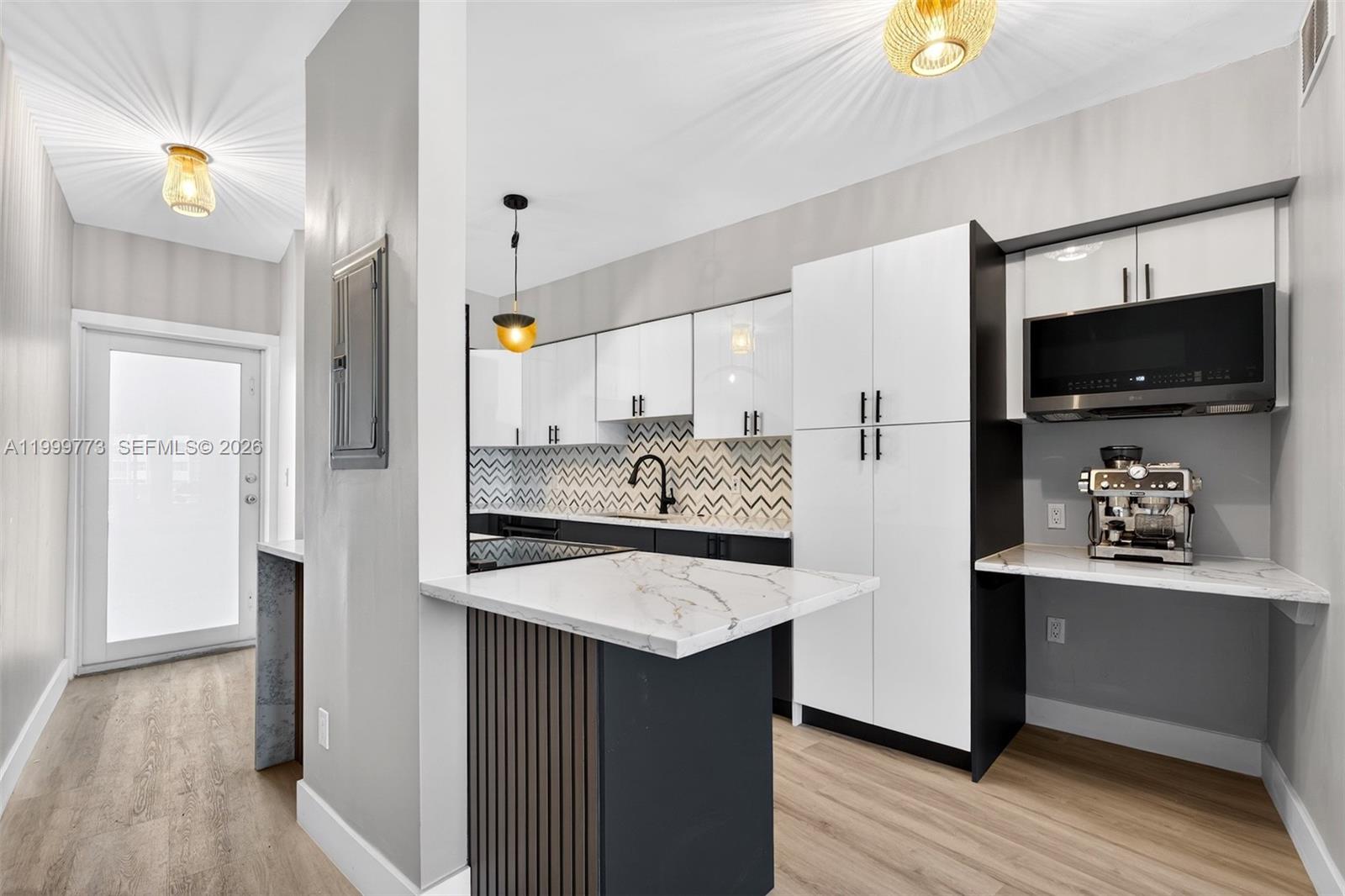 A modern kitchen features white cabinets, a marble-topped island, and a chevron-patterned backsplash — 2500 Diana Dr # 216, Hallandale Beach FL 33009, HALLANDALE BEACH, FL