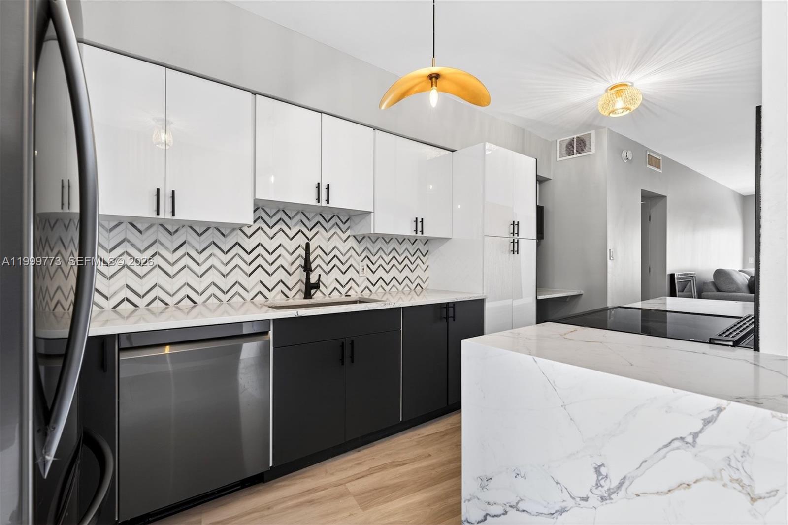 A modern kitchen features white upper cabinets, black lower cabinets, and a marble-patterned island — 2500 Diana Dr # 216, Hallandale Beach FL 33009, HALLANDALE BEACH, FL