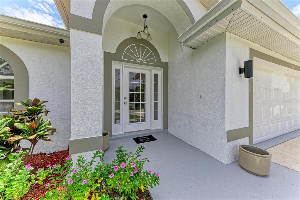 A white front door with sidelights and a transom window sits under a covered entryway — 3081 JODY STREET, PORT CHARLOTTE, FL