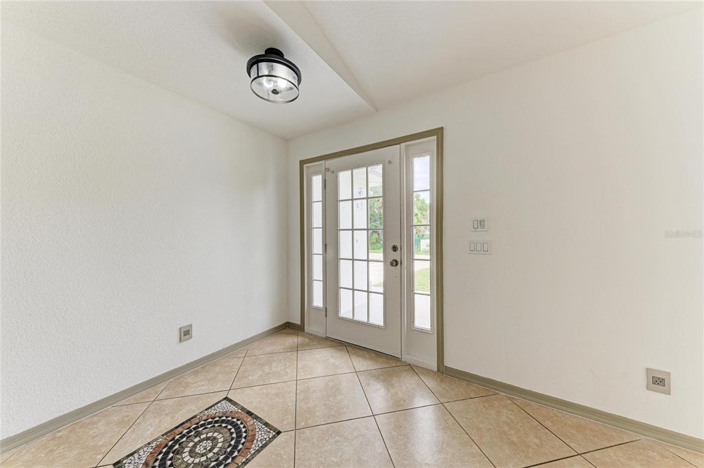 An entryway features beige tile flooring, a decorative mosaic inlay, and a glass-paneled front door — 3081 JODY STREET, PORT CHARLOTTE, FL