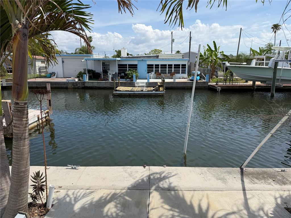 A view of a canal-front house with a dock, patio, and boat from a concrete seawall — 6736 CURLEW LANE, HUDSON, FL