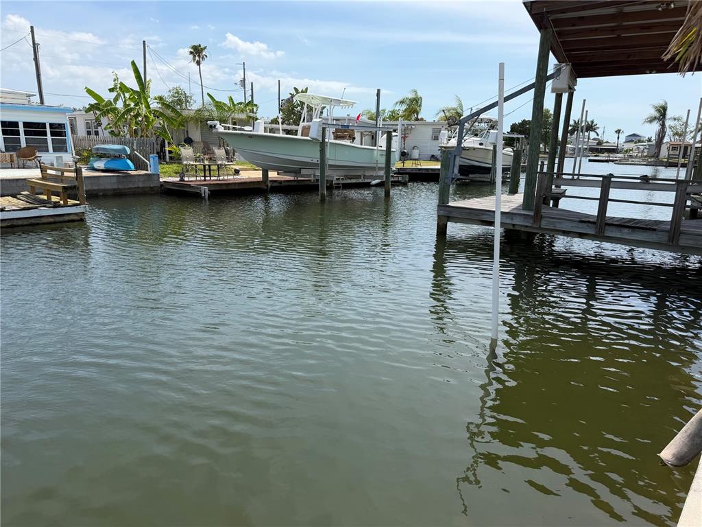 A canal view shows a boat on a lift next to a wooden dock — 6736 CURLEW LANE, HUDSON, FL