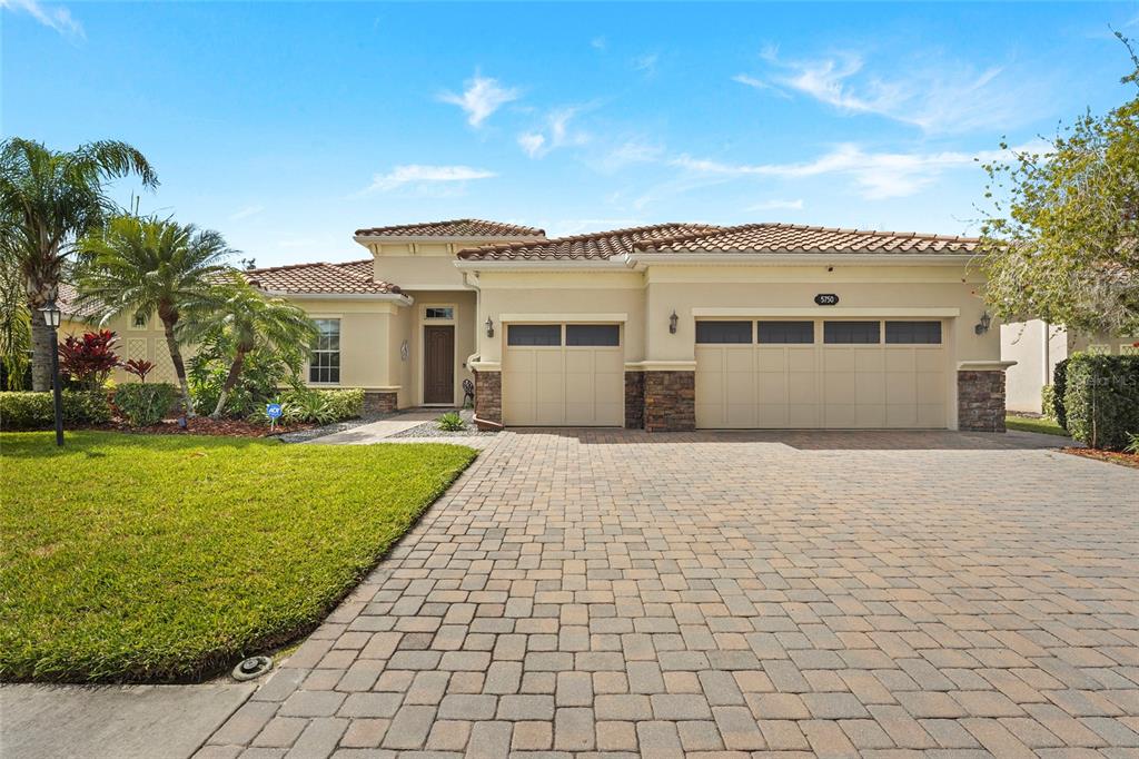 A single-story house with a tiled roof, beige stucco walls, and a stone-accented three-car garage — 5750 ROCK DOVE DRIVE, SARASOTA, FL