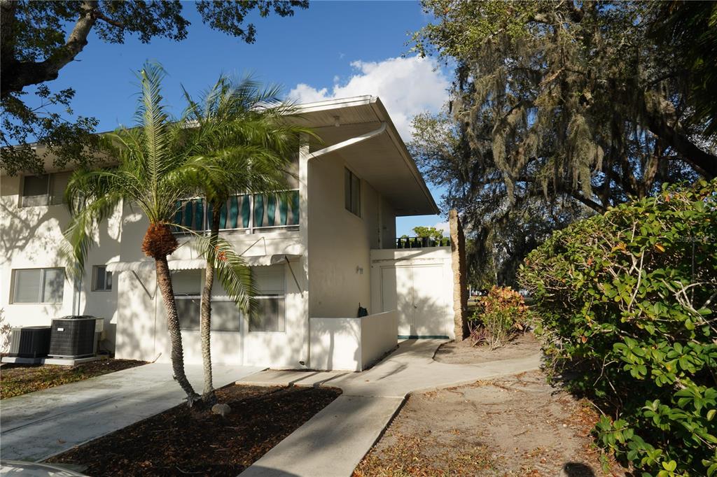 A two-story stucco building with a palm tree, a concrete walkway, and mature trees — 349 JOEL BOULEVARD UNIT 201, LEHIGH ACRES, FL