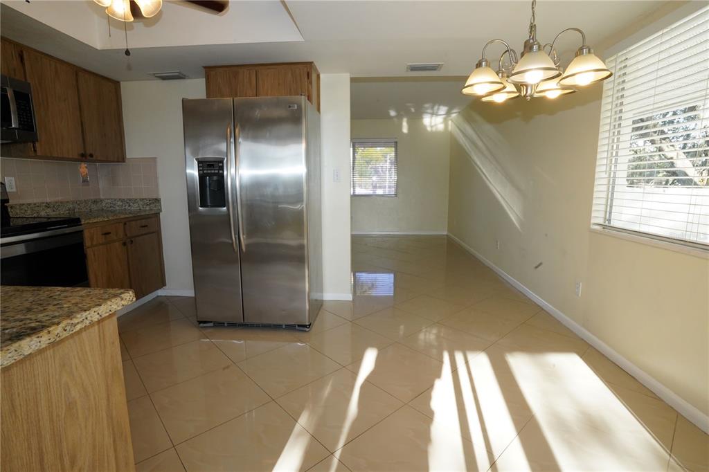 A kitchen with wood cabinets, granite countertops, and stainless steel appliances opens to a dining area — 349 JOEL BOULEVARD UNIT 201, LEHIGH ACRES, FL