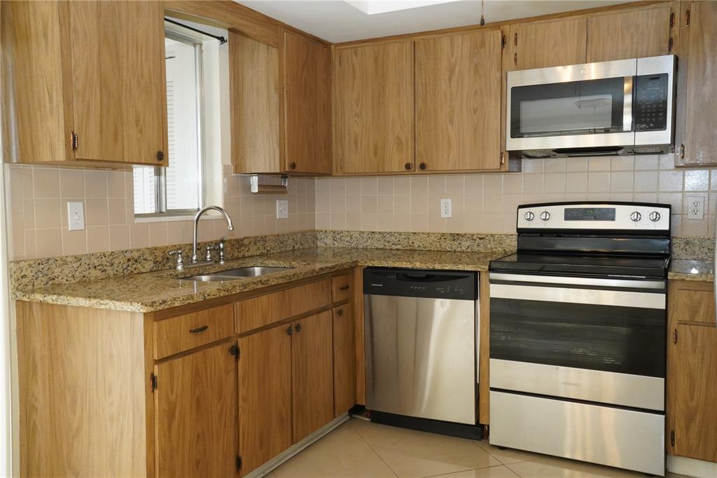 A kitchen with wood cabinets, granite countertops, stainless steel appliances, and beige tile backsplash — 349 JOEL BOULEVARD UNIT 201, LEHIGH ACRES, FL