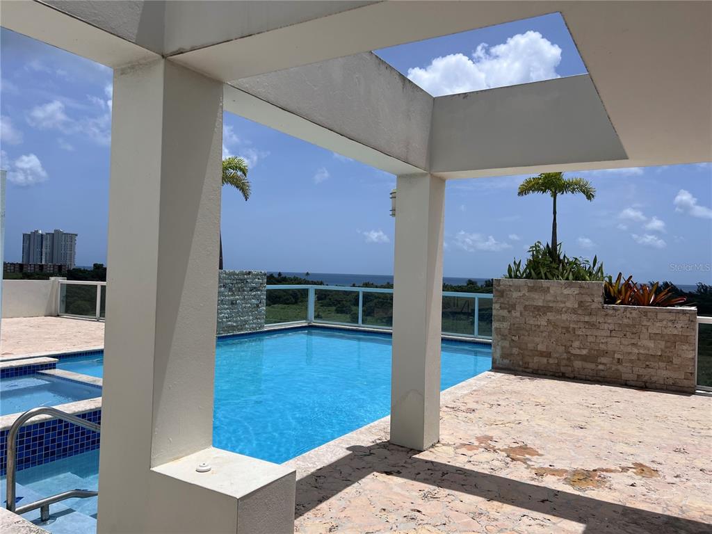 A swimming pool with a glass railing overlooks the ocean from a stone-paved terrace — 100 OCEAN PLAZA DRIVE UNIT 15, LUQUILLO, PR