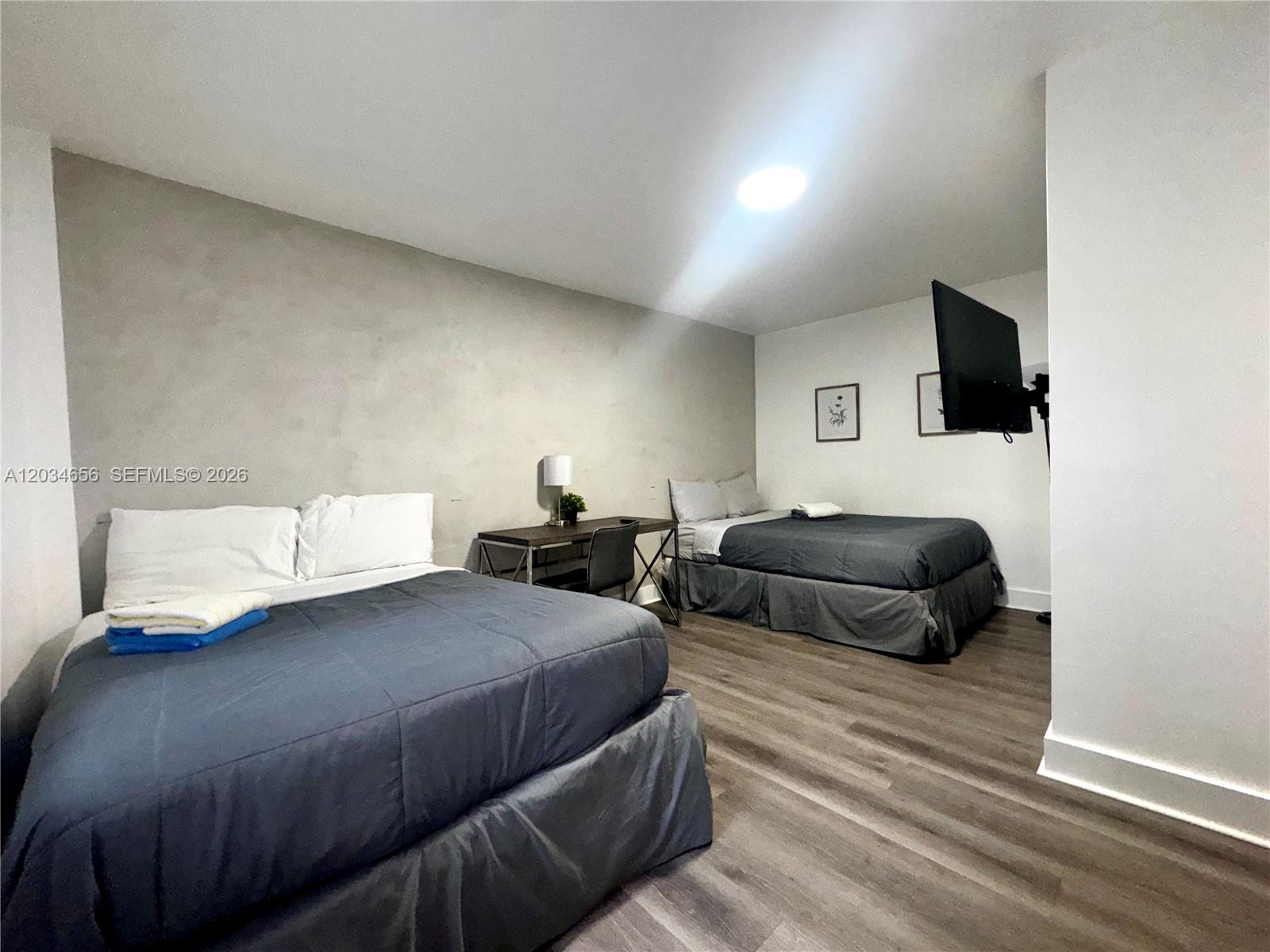 A bedroom features two beds, a desk, and a wall-mounted television on wood-look flooring — 1684 SW 10th St, Miami FL 33135, MIAMI, FL