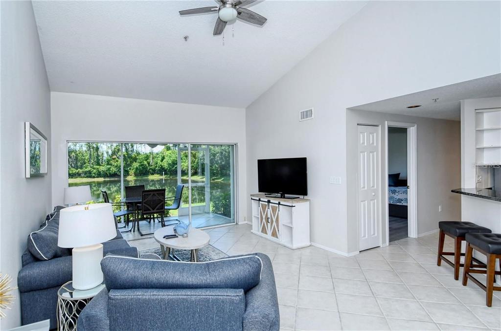 A living room with tile floors, a vaulted ceiling, and a sliding door to a patio — 5414 FAIR OAKS STREET UNIT 10-D, BRADENTON, FL