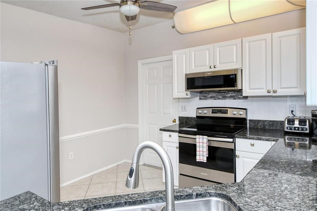 A kitchen with white cabinets, stainless steel appliances, and dark granite countertops — 5414 FAIR OAKS STREET UNIT 10-D, BRADENTON, FL